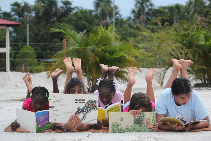 Vijf kinderen lezen samen boeken in het zand
